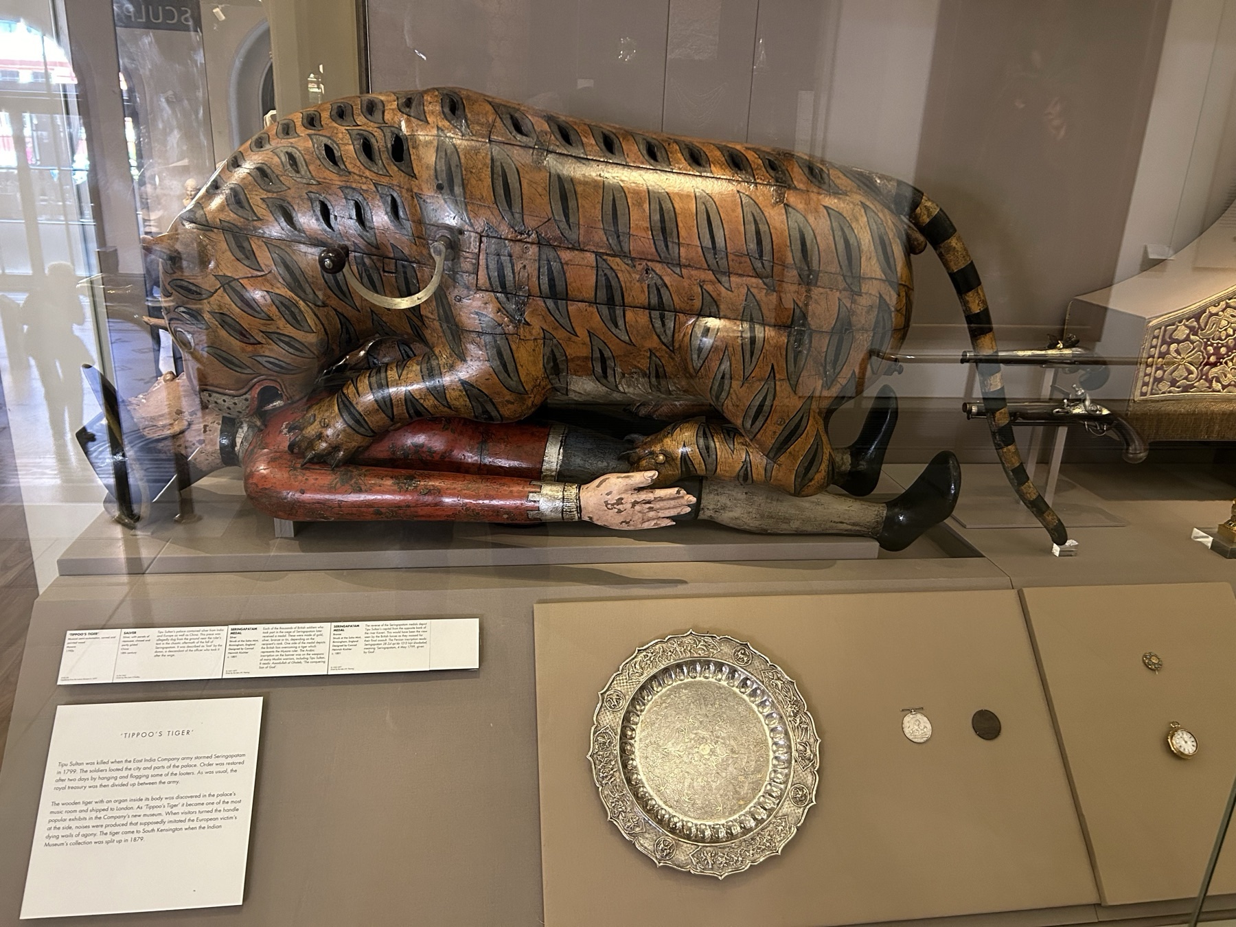 Tipu's tiger, a life-sized painted wooden automaton of a tiger mauling a red-coated European soldier, displayed in a glass case at the Victoria and Albert Museum.